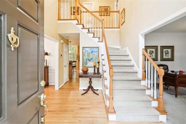 foyer with light wood-type flooring, baseboards, a high ceiling, and stairs