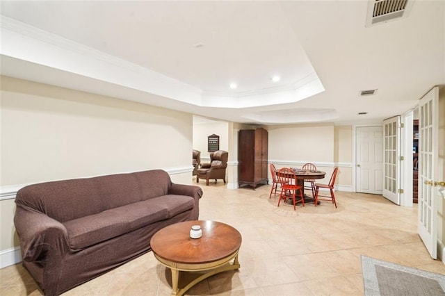 living room featuring a tray ceiling, visible vents, and ornamental molding