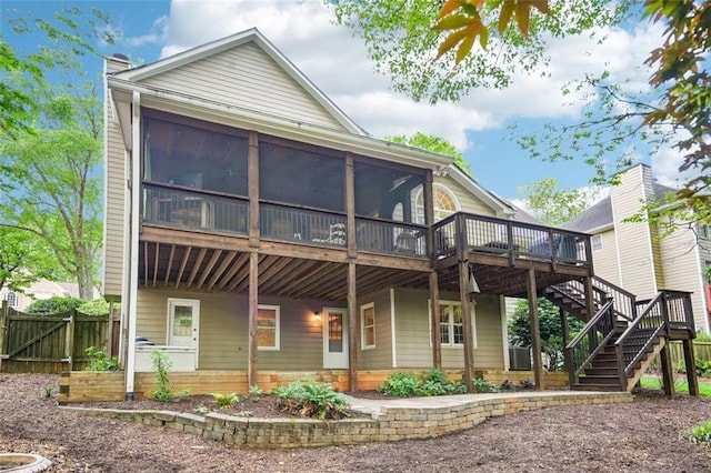 rear view of house with stairway, a wooden deck, fence, and a sunroom