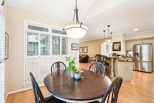 dining area with vaulted ceiling, baseboards, ornamental molding, and light wood-style floors