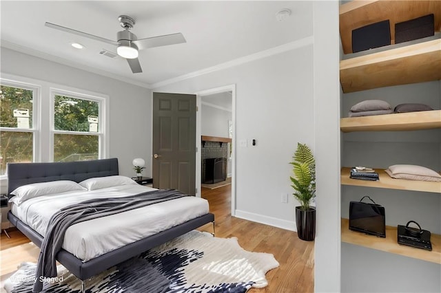 bedroom with light wood-style floors, a fireplace, baseboards, and crown molding