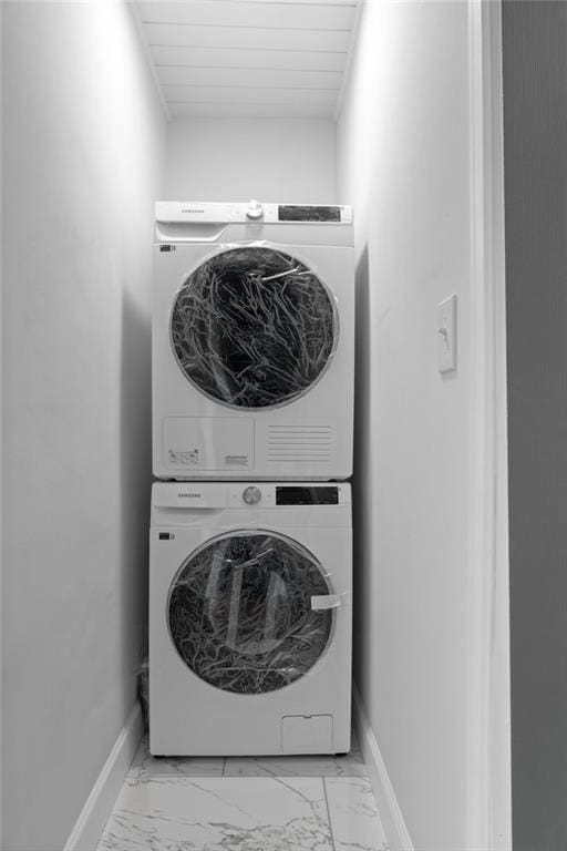 laundry room featuring stacked washer / drying machine, marble finish floor, baseboards, and laundry area