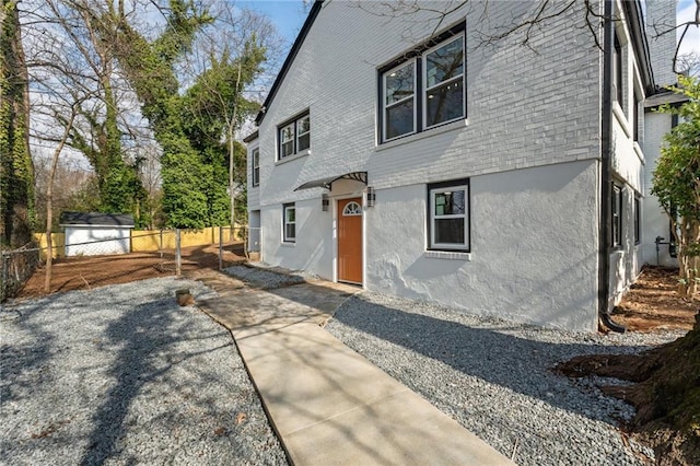 back of house featuring an outbuilding, a storage unit, fence, and stucco siding