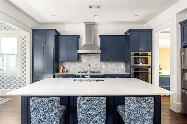 kitchen with a center island with sink, a kitchen breakfast bar, and wall chimney range hood