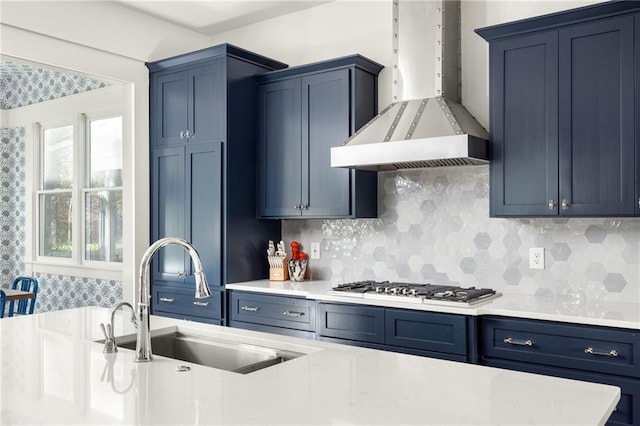 kitchen featuring sink, wall chimney exhaust hood, blue cabinetry, tasteful backsplash, and stainless steel gas cooktop