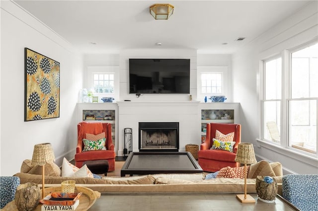 living room featuring a large fireplace, crown molding, and plenty of natural light