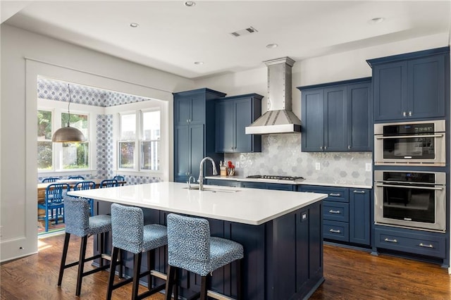 kitchen with a center island with sink, wall chimney exhaust hood, dark hardwood / wood-style floors, and blue cabinets