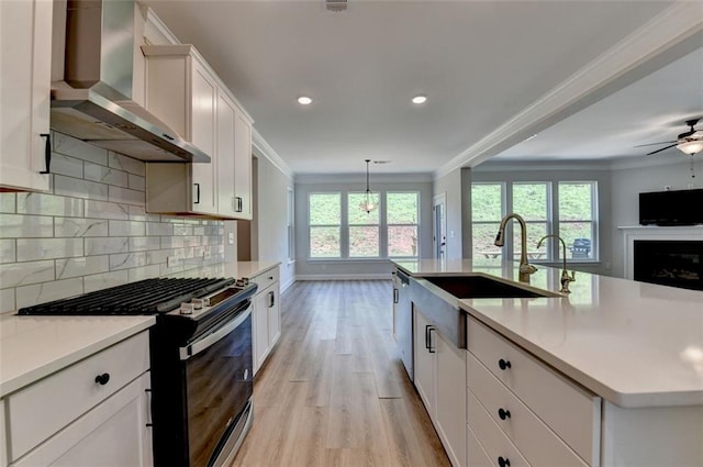 6867 Kate Ln, Flowery Branch, GA 30542 - kitchen with wall chimney exhaust hood, range with gas cooktop, ornamental molding, light wood finished floors, and light countertops