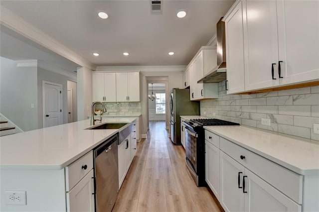 6867 Kate Ln, Flowery Branch, GA 30542 - kitchen featuring stainless steel appliances, ornamental molding, wall chimney range hood, light wood-style floors, and white cabinetry