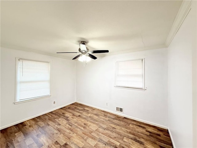 spare room featuring a ceiling fan, wood finished floors, baseboards, visible vents, and crown molding