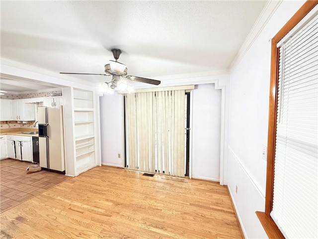 unfurnished living room featuring visible vents, a sink, light wood-style floors, crown molding, and ceiling fan