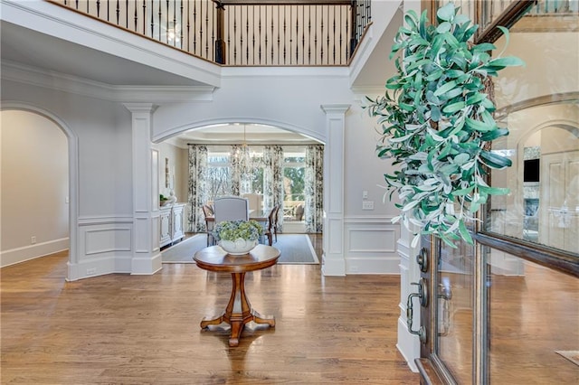 foyer featuring arched walkways, a notable chandelier, a decorative wall, wood finished floors, and crown molding