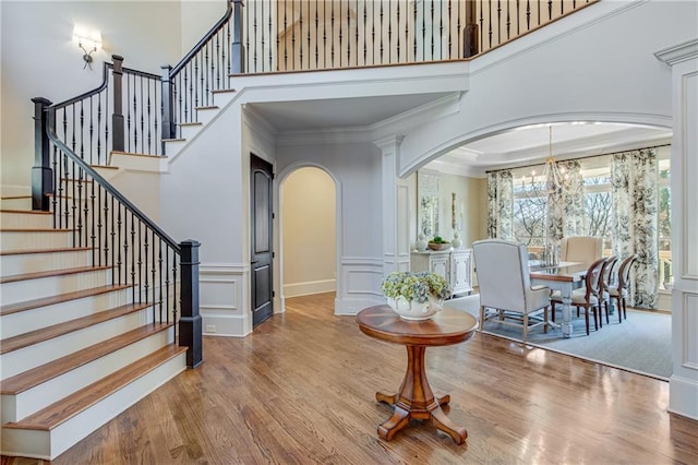 foyer with arched walkways, a towering ceiling, ornamental molding, wood finished floors, and a decorative wall