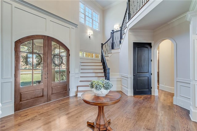 foyer entrance featuring arched walkways, french doors, crown molding, stairway, and light wood-type flooring