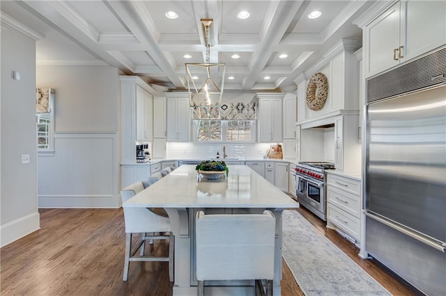 kitchen featuring premium appliances, a breakfast bar, beam ceiling, white cabinets, and a sink