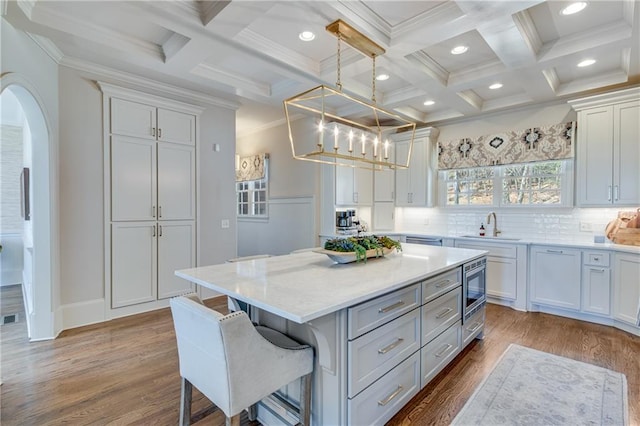 kitchen with arched walkways, white cabinets, stainless steel microwave, light countertops, and a sink