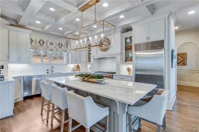 kitchen with stainless steel appliances, white cabinetry, beam ceiling, a center island, and a kitchen bar