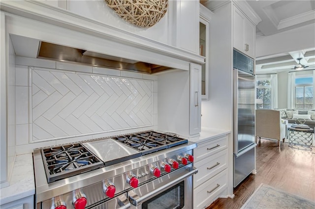 kitchen with tasteful backsplash, high end appliances, dark wood finished floors, custom exhaust hood, and white cabinetry