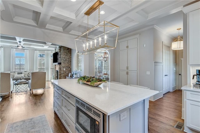 kitchen with decorative light fixtures, a fireplace, stainless steel microwave, dark wood-type flooring, and open floor plan