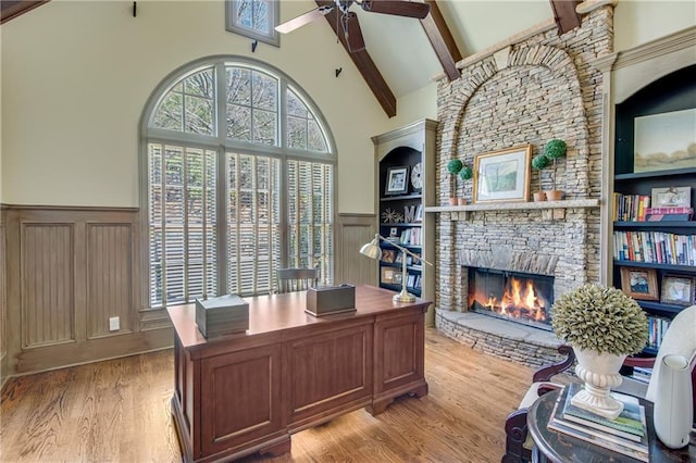 office space featuring wainscoting, beamed ceiling, light wood-type flooring, a fireplace, and high vaulted ceiling