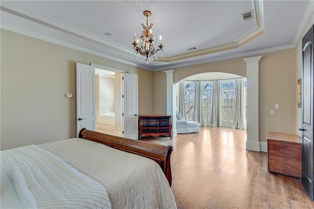 bedroom featuring crown molding, a tray ceiling, decorative columns, and light wood finished floors