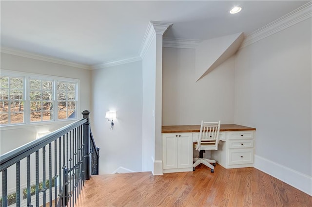 office area with light wood-type flooring, baseboards, ornamental molding, and built in desk