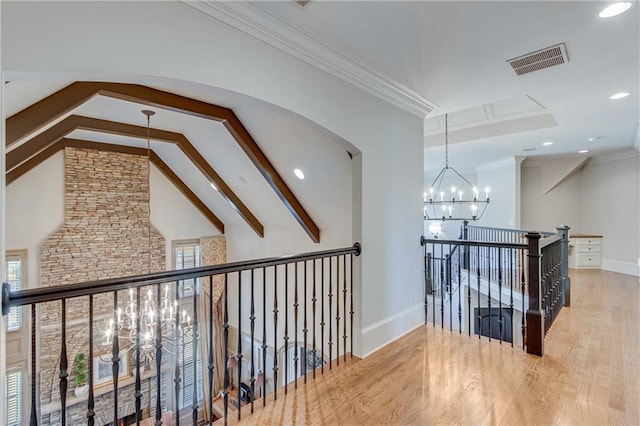 corridor with visible vents, ornamental molding, wood finished floors, beamed ceiling, and a chandelier