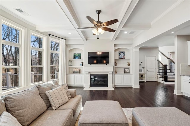 living area with dark wood-style floors, beam ceiling, visible vents, a glass covered fireplace, and coffered ceiling