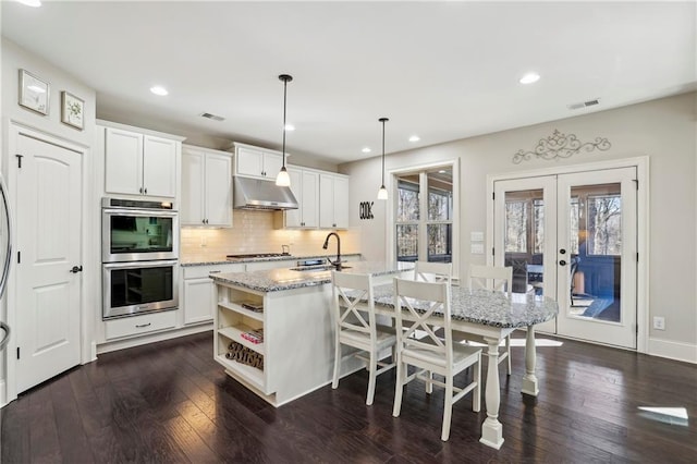 kitchen with hanging light fixtures, under cabinet range hood, white cabinetry, and open shelves