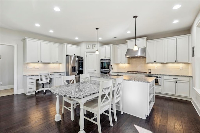 kitchen with white cabinets, under cabinet range hood, appliances with stainless steel finishes, and pendant lighting