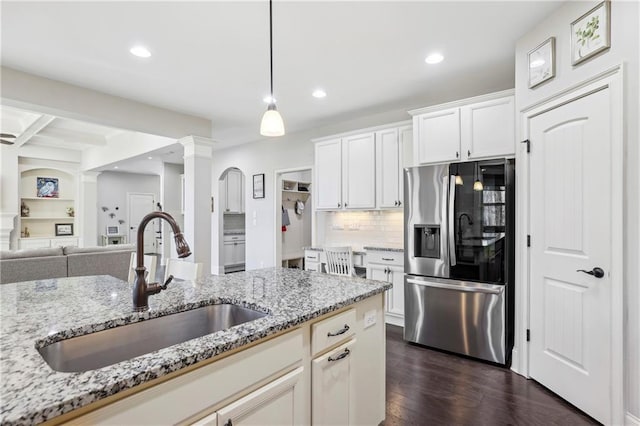 kitchen featuring stainless steel fridge, light stone counters, open floor plan, white cabinetry, and a sink