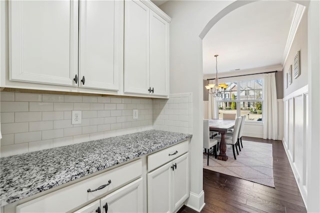 kitchen featuring arched walkways, backsplash, dark wood-type flooring, white cabinetry, and light stone countertops