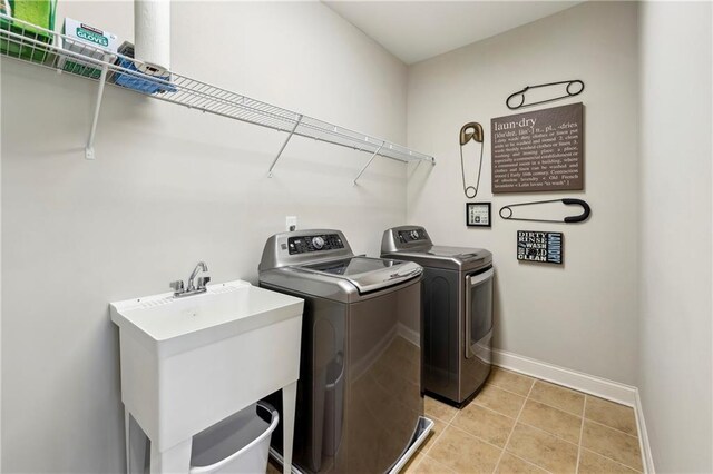 laundry room with laundry area, light tile patterned floors, baseboards, washing machine and clothes dryer, and a sink