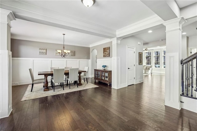 dining room featuring decorative columns, dark wood finished floors, wainscoting, crown molding, and a decorative wall