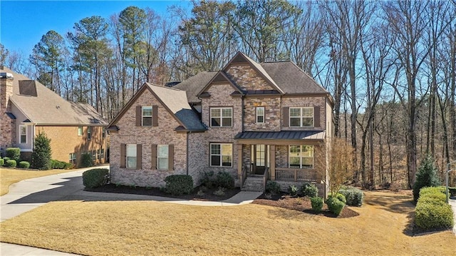 craftsman-style house featuring covered porch, a standing seam roof, brick siding, and a front yard