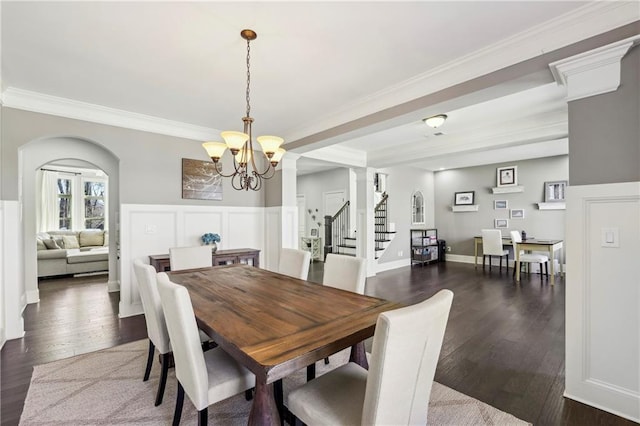 dining room featuring stairs, ornamental molding, arched walkways, and dark wood-type flooring