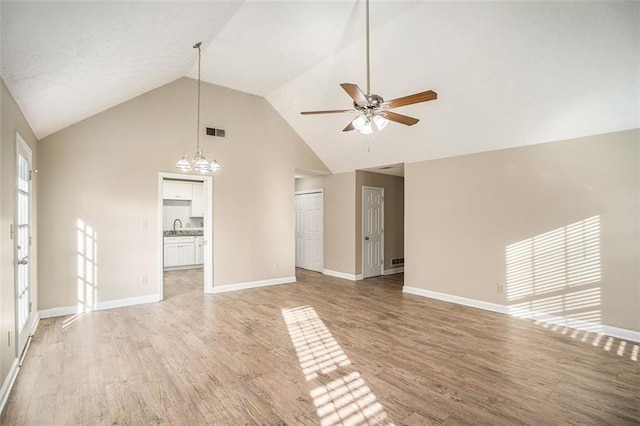 unfurnished living room with ceiling fan with notable chandelier, wood-type flooring, high vaulted ceiling, and sink