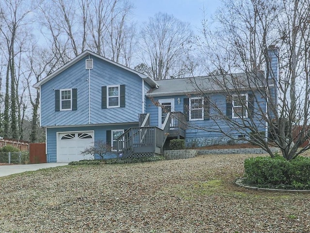 split level home with concrete driveway, fence, a garage, and a chimney