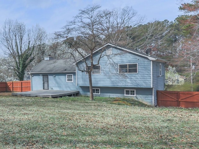 rear view of house with a deck, fence, a lawn, and a chimney