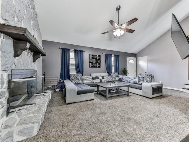 living area with baseboards, vaulted ceiling, carpet flooring, a stone fireplace, and a ceiling fan