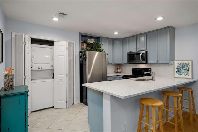 1445 Monroe Dr NE Unit C13, Atlanta, GA 30324 - kitchen with appliances with stainless steel finishes, stacked washing machine and dryer, gray cabinets, a peninsula, and decorative backsplash