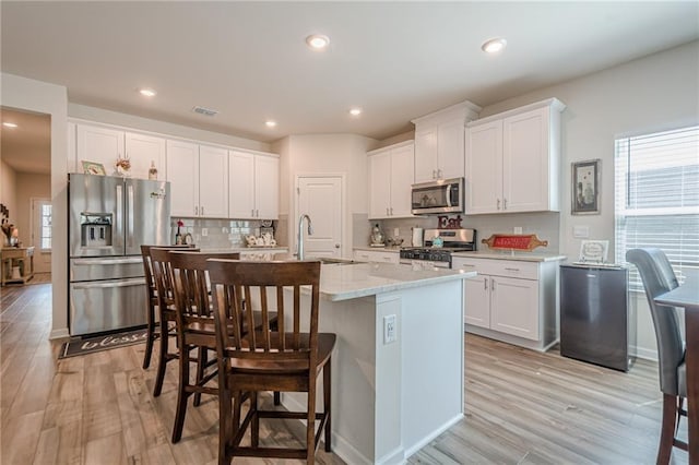 kitchen with stainless steel appliances, a sink, light wood-type flooring, a kitchen island with sink, and white cabinetry