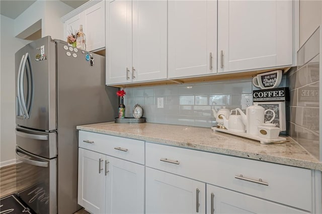 kitchen featuring tasteful backsplash, white cabinets, freestanding refrigerator, and light stone countertops