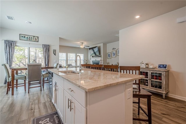 kitchen with a sink, a kitchen bar, a fireplace, open floor plan, and white cabinetry