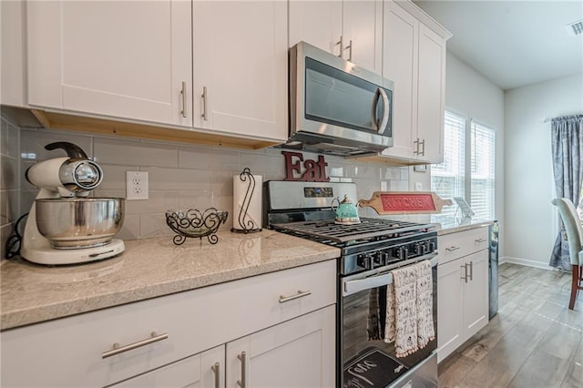 kitchen featuring stainless steel appliances, white cabinetry, light stone countertops, and tasteful backsplash