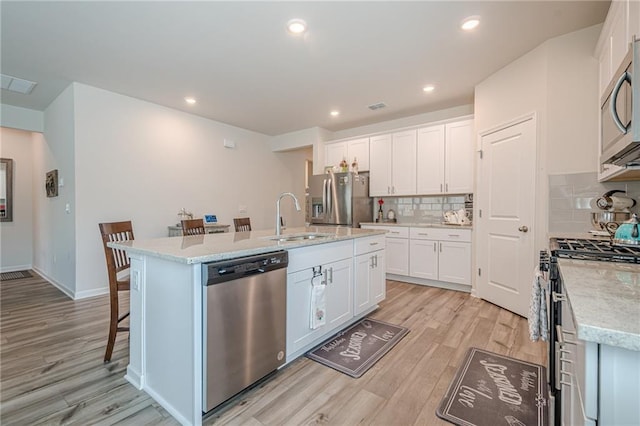 kitchen with appliances with stainless steel finishes, a sink, light wood-style floors, white cabinets, and recessed lighting