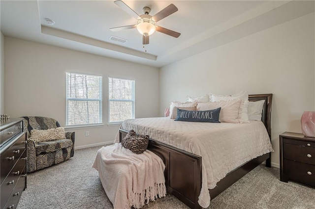 bedroom featuring light carpet, baseboards, ceiling fan, and a tray ceiling