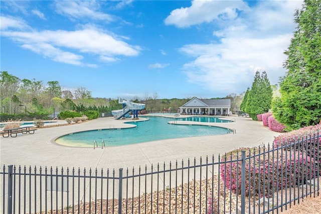 community pool with a water slide, fence, and a patio