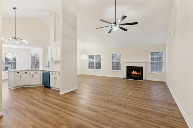 unfurnished living room with ceiling fan with notable chandelier, high vaulted ceiling, sink, and hardwood / wood-style floors