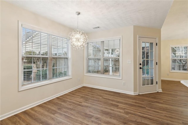 unfurnished dining area featuring a notable chandelier, dark wood-type flooring, and a textured ceiling